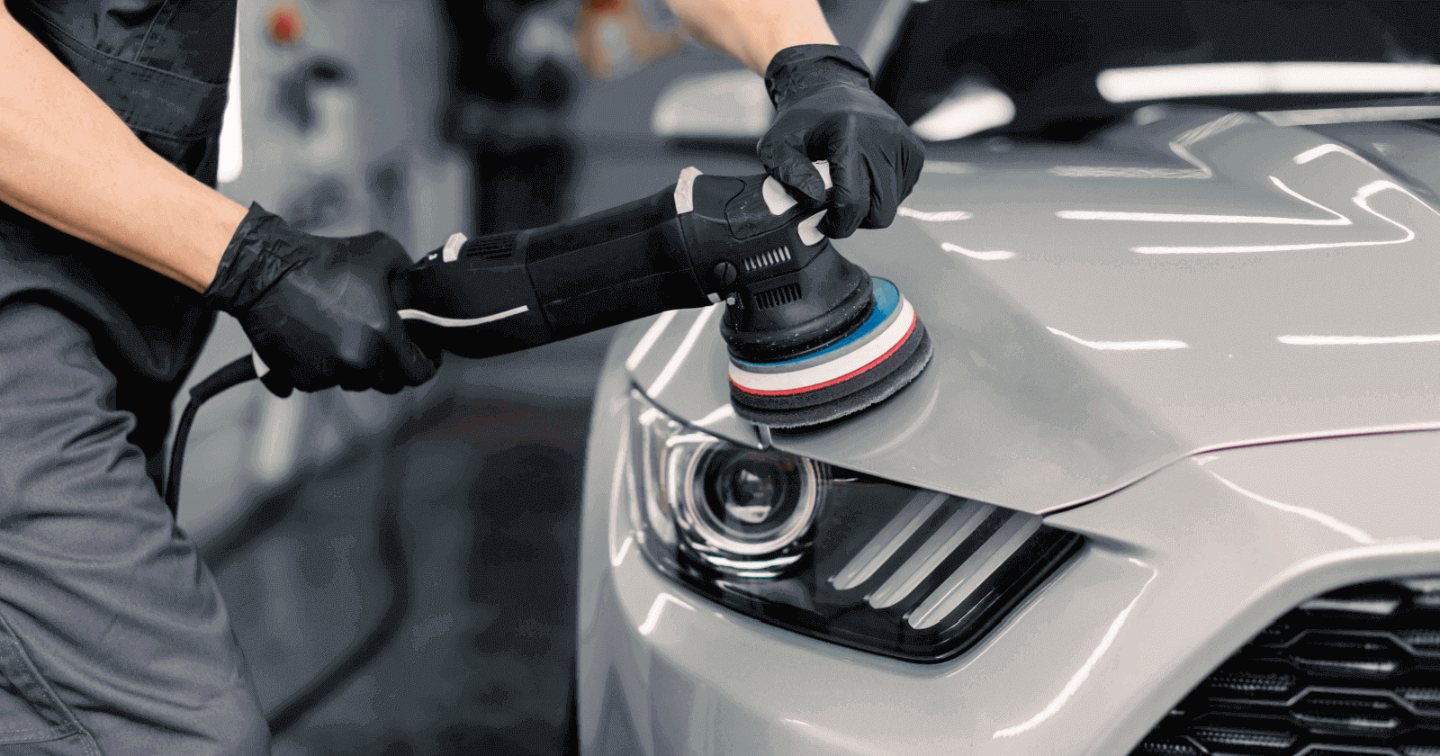 A dual-action polisher working across the front fender of a gray car.